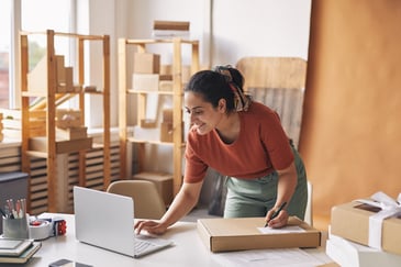 small business owner - woman in home office smiling at computer while filling out address on product package
